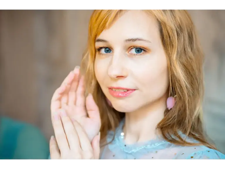 Close-up indoor portrait of a woman with long brown hair and pink earrings embracing a sheer beauty look.