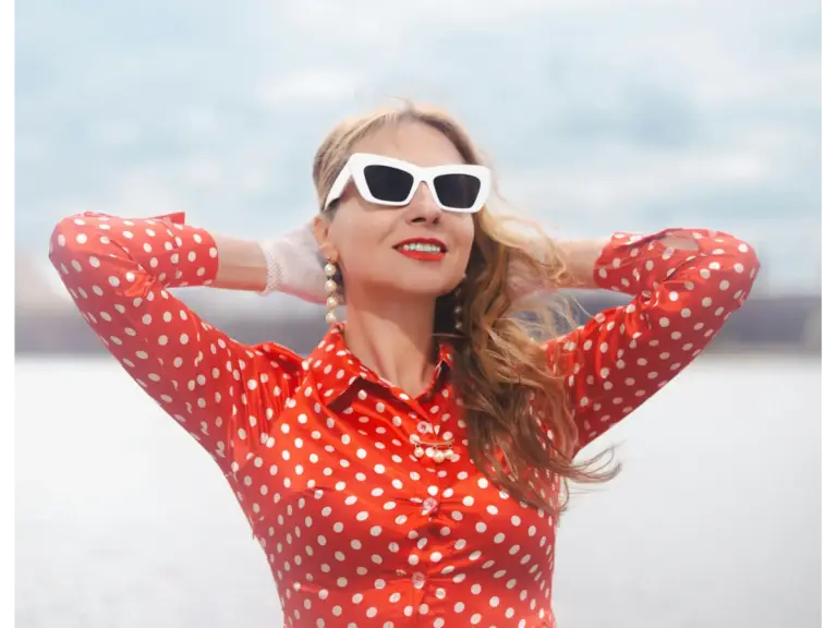 Stylish woman in a red polka dot dress with sunglasses enjoying a sunny day outdoors, effortlessly showcasing the charm of polka dots in warm weather.