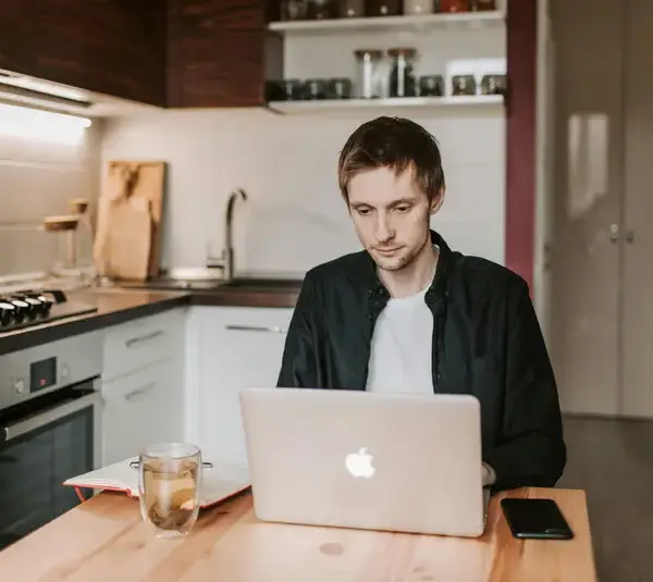 A young man using a laptop in a cozy kitchen, illustrating remote work lifestyle.
