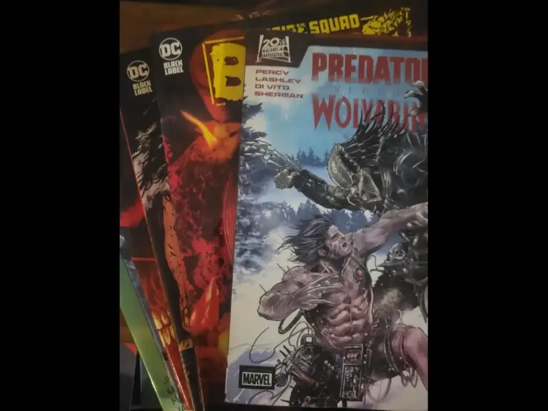 A stack of graphic novels featuring Predator versus Wolverine on top, laid out next to other comic books.