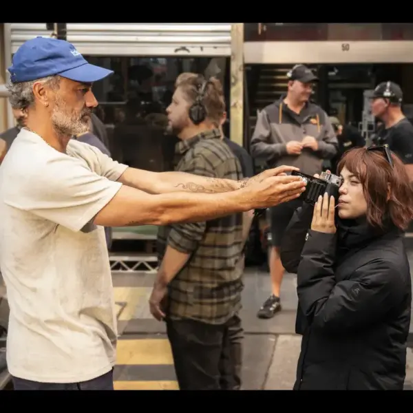 Taika Waititi blocking Jenna Ortega from looking through a camera lens.