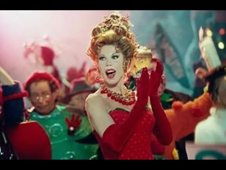 Actress Christine Baranski costumed as Martha May Whovier in How the Grinch Stole Christmas, with a Beehive Hair Style, Gold and Red Necklace, Red Dress with white dots, and Red Elbow length Gloves