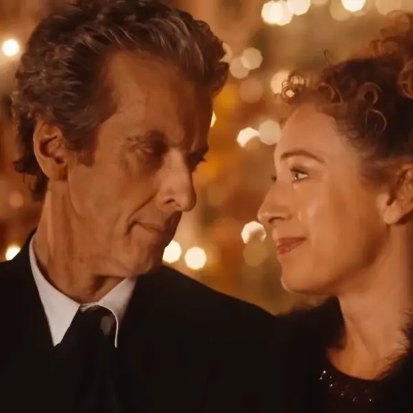Doctor Who 2015 Christmas special The Husbands of River Song where The Doctor, played by Peter Capaldi, and a River Song, played by Alex stand closely, gazing at each other with warm smiles. The background is softly blurred with glowing lights, creating a cozy, intimate atmosphere.