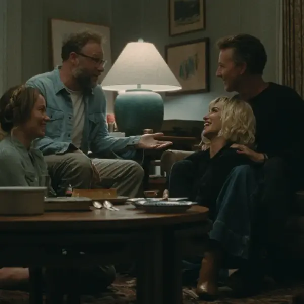 The cast of A24's "The Invite" are seated at a table in a living room, sharing ideas and enjoying each other's company.