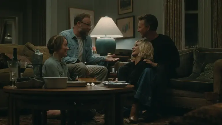 The cast of A24's "The Invite" are seated at a table in a living room, sharing ideas and enjoying each other's company.