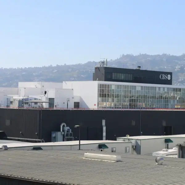 A large CBS studio building with modern architecture, featuring white and black exterior tones, set against a backdrop of distant hills and a clear sky. CBS has announced its 2027 show cancellations.