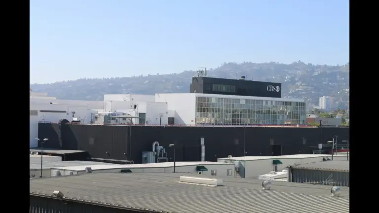 A large CBS studio building with modern architecture, featuring white and black exterior tones, set against a backdrop of distant hills and a clear sky. CBS has announced its 2027 show cancellations.