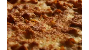 a close-up of baked ziti topped with golden, bubbly melted cheese, showing a perfectly crisp and browned surface fresh from the oven.