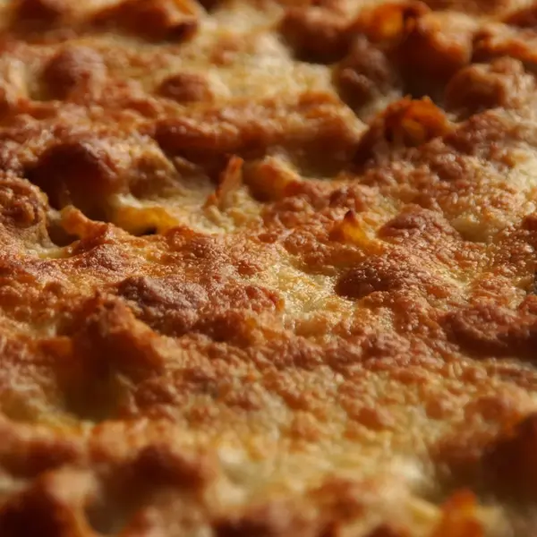 a close-up of baked ziti topped with golden, bubbly melted cheese, showing a perfectly crisp and browned surface fresh from the oven.