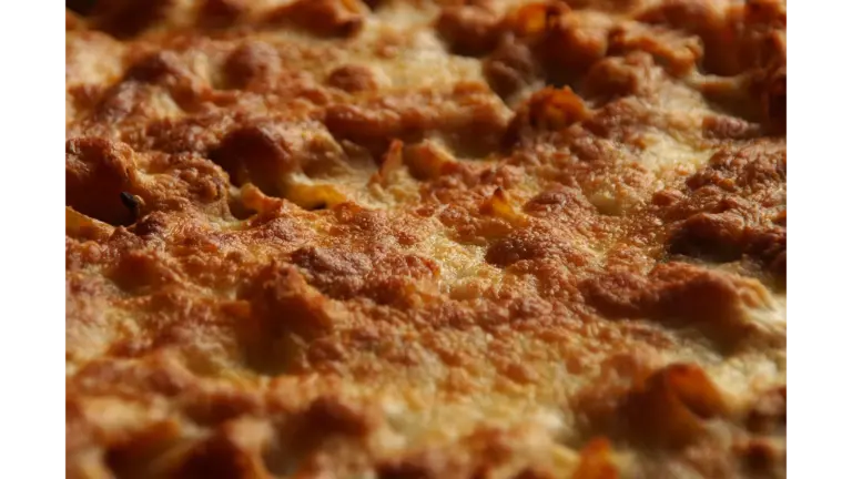 a close-up of baked ziti topped with golden, bubbly melted cheese, showing a perfectly crisp and browned surface fresh from the oven.