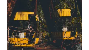 Eerie scene of an abandoned Ferris wheel in Chernobyl with a lone woman standing beneath it, highlighting the haunting beauty of abandoned parks.
