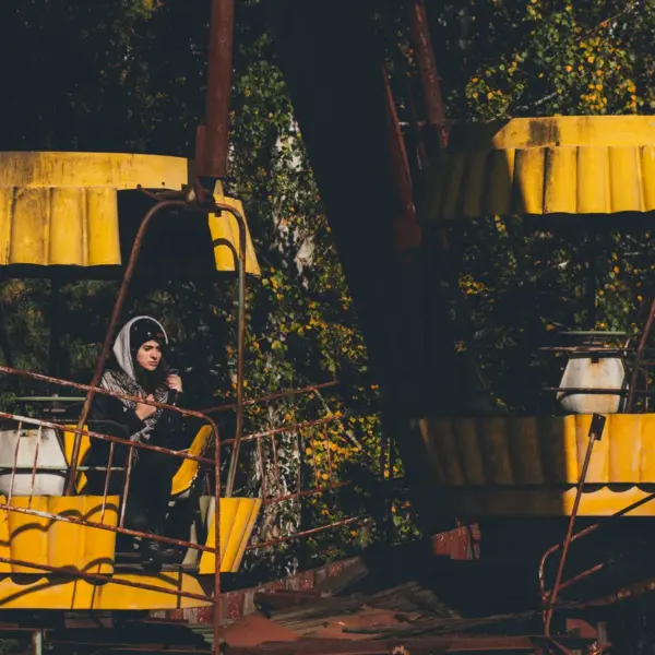 Eerie scene of an abandoned Ferris wheel in Chernobyl with a lone woman standing beneath it, highlighting the haunting beauty of abandoned parks.