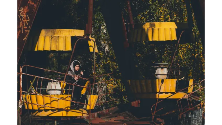 Eerie scene of an abandoned Ferris wheel in Chernobyl with a lone woman standing beneath it, highlighting the haunting beauty of abandoned parks.