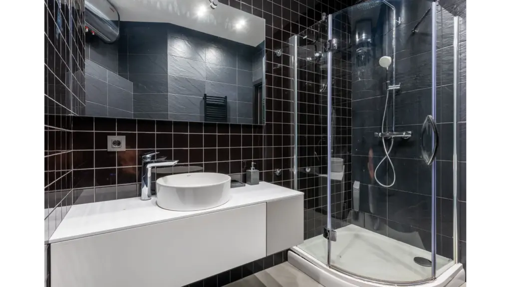 Bathroom tiles elevate this stylish bathroom with black tile walls, a glass shower, and sleek modern fixtures