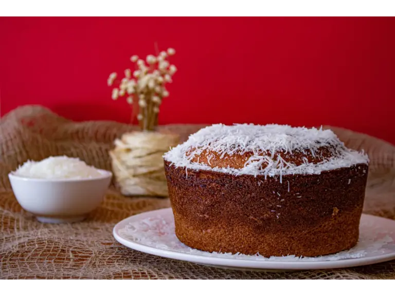 A mouthwatering homemade coconut cake with shredded coconut topping against a vibrant red backdrop.