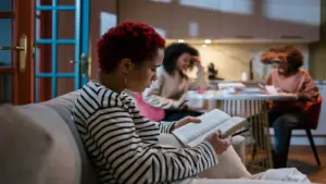 In daly devotional, young women sit around studying the Bible at a kitchen table and couch.