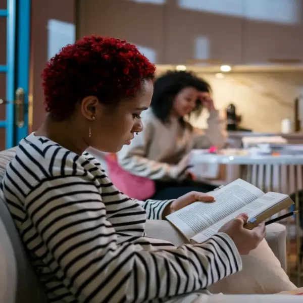 In daly devotional, young women sit around studying the Bible at a kitchen table and couch.