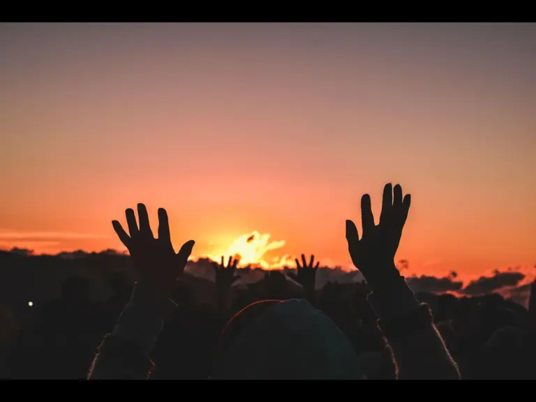 In daly devotional, people are lifting their handsw to God in prayer as the sun rises.