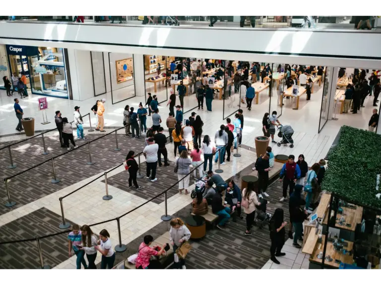 travel chaos fills a bustling shopping center as a huge crowd queues inside an Apple Store during a packed retail rush.