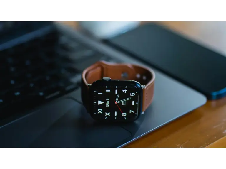 A modern smart luxury watch with a brown leather band sits on a laptop, showcasing sleek technology design.