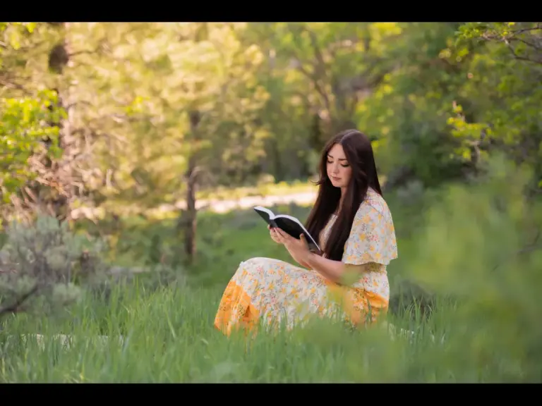 In daily devotional, a young woman sits in a meadow reading the Bible.