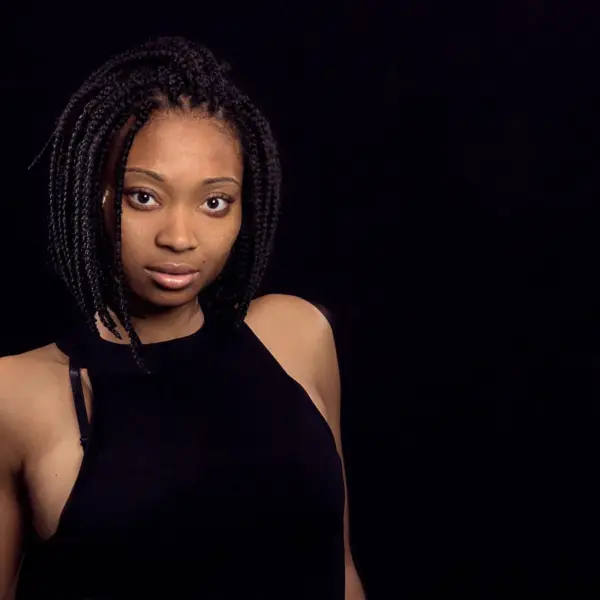 a stunning portrait of a Black woman with braided hair, exuding confidence against a dark background, beautifully highlighting the bold, structured look of bob braids.