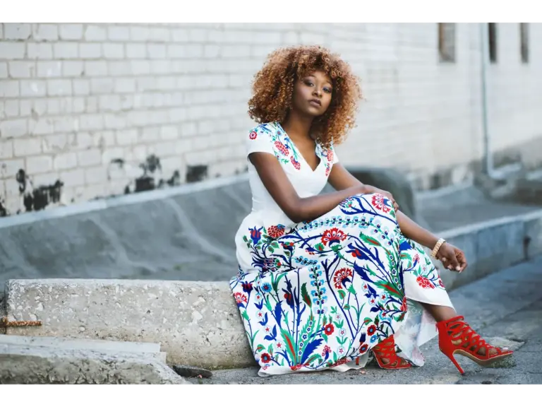 African American woman sitting and posing in one of vibrant floral dresses against a brick wall