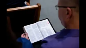 In daily devotional, a man is reading the Bible intently while sitting on a church pew.