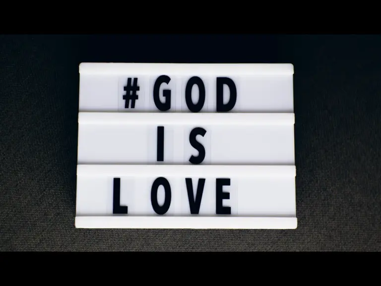 In daily devotional, a white "God is Love" sign is displayed against a black background