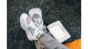 White sneakers casually placed on grass with an open book, conveying a relaxed outdoor vibe that pairs perfectly with the laid‑back style of dad sneakers.