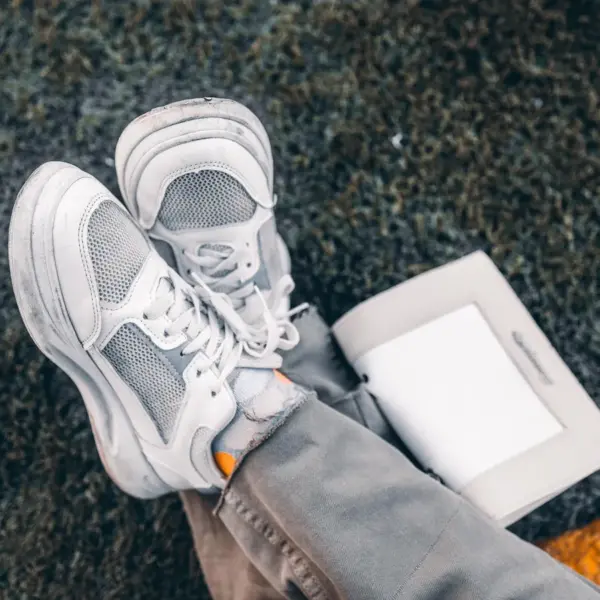 White sneakers casually placed on grass with an open book, conveying a relaxed outdoor vibe that pairs perfectly with the laid‑back style of dad sneakers.
