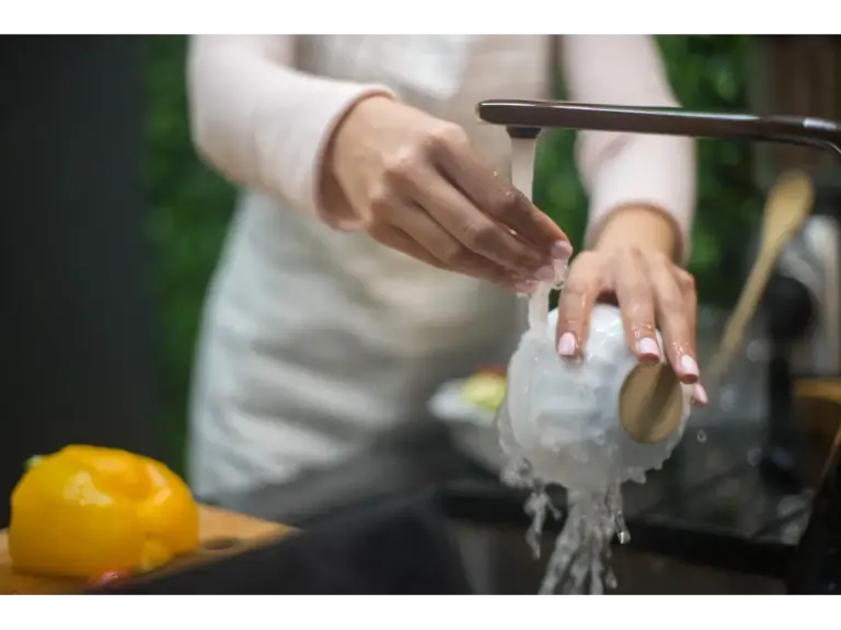 Close‑up of hands washing a white bowl under a running faucet in a kitchen, capturing a simple moment of everyday home cleaning