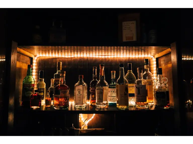 A stylish arrangement of various vintage liquor bottles beautifully illuminated on a shelf in a dimly lit bar setting.