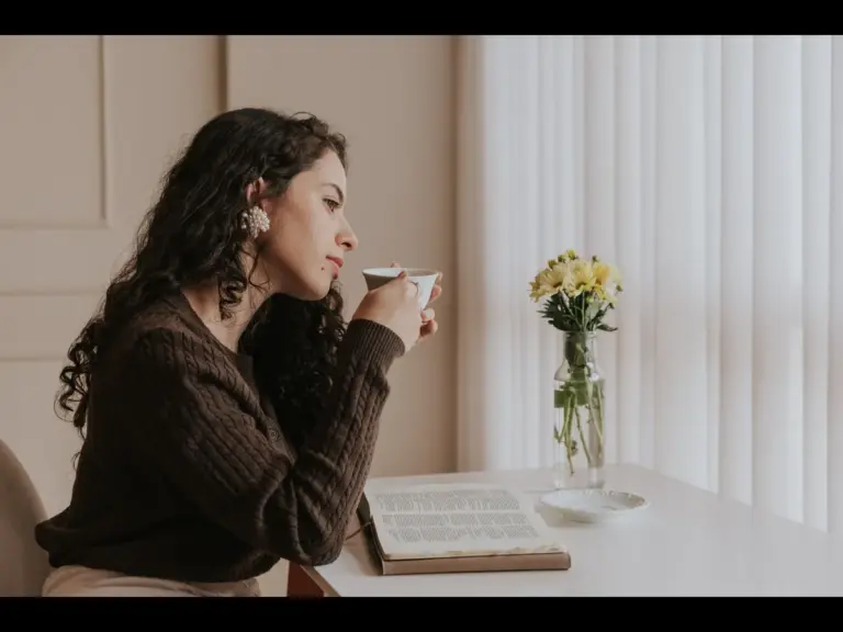 In daily devotional, a woman is sitting at a table with an open bible as she seems to meditate on God's word.