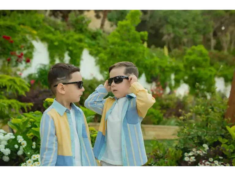 Sibling style shines as two children wearing sunglasses and matching outfits enjoy a sunny day in a lush, vibrant garden.