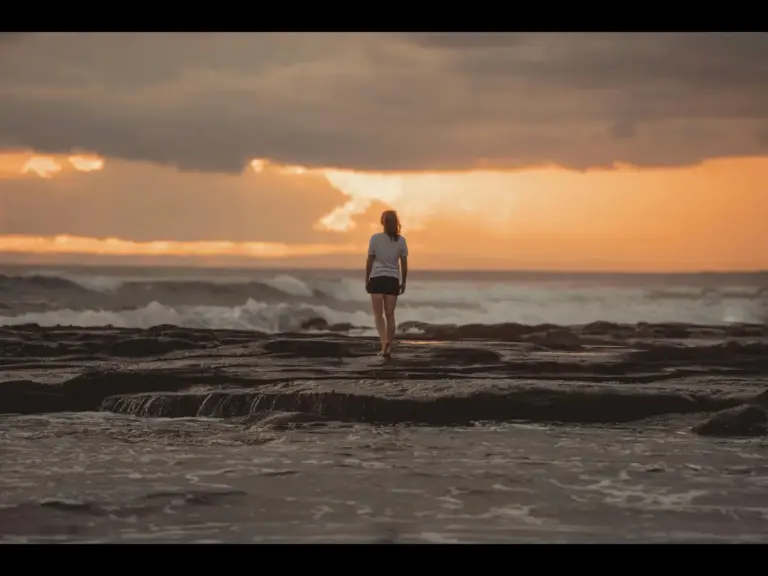 In daily devotional, a woman stands alone on a beach during a sunset.