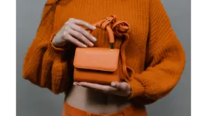 A woman holds an orange leather mini handbag against an orange sweater in a studio setting, echoing the bold charm of mini bucket bags.