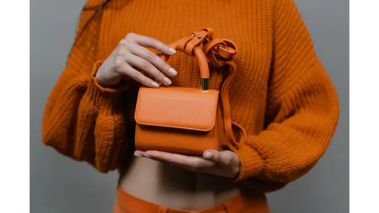 A woman holds an orange leather mini handbag against an orange sweater in a studio setting, echoing the bold charm of mini bucket bags.