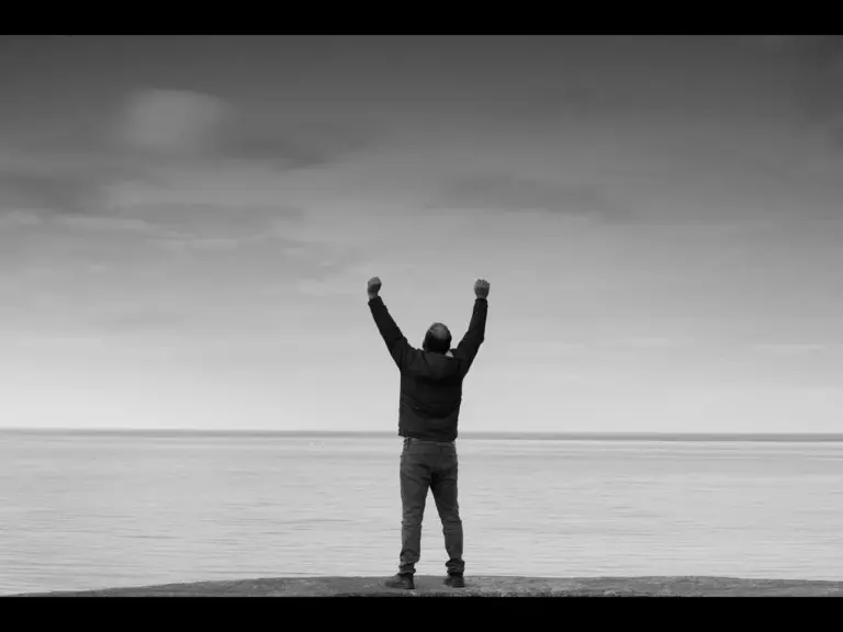 In daily devotional, a man with raised arms in victoroy is shown against a gray sky.