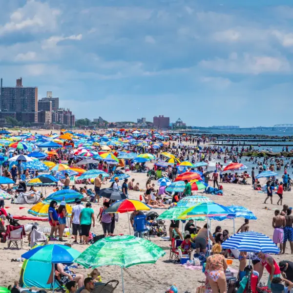 travel chaos unfolds at Coney Island as a vibrant summer scene shows beachgoers, umbrellas, and the shoreline packed with energy.