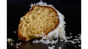 A detailed image of a coconut cake slice on a black background, highlighting texture.