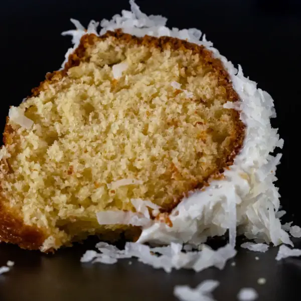 A detailed image of a coconut cake slice on a black background, highlighting texture.
