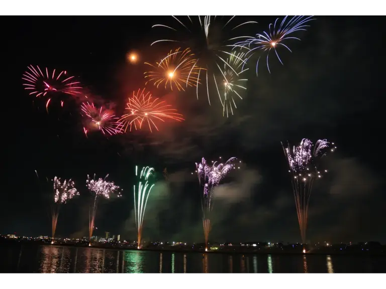 Colorful beach fireworks illuminate the night sky, reflecting beautifully on a river and capturing a festive celebration.