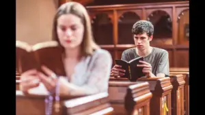 In daily devotional, a man and woman sit on church pews readng the Bible.