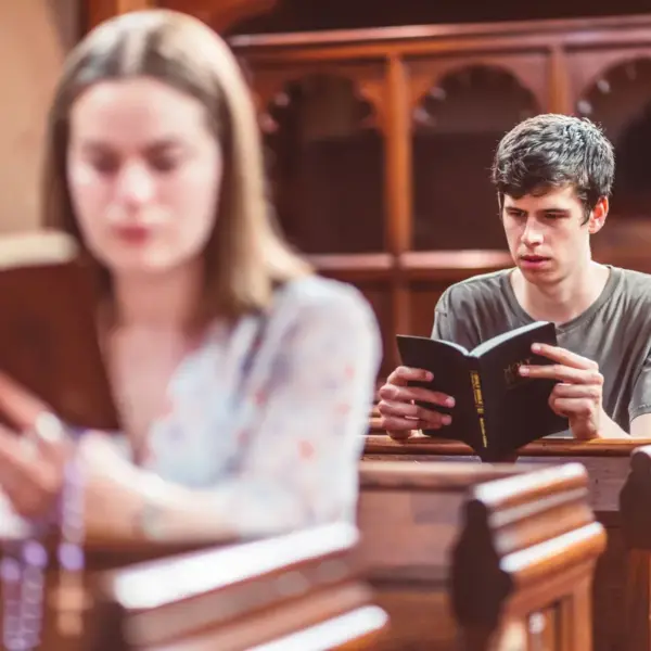 In daily devotional, a man and woman sit on church pews readng the Bible.