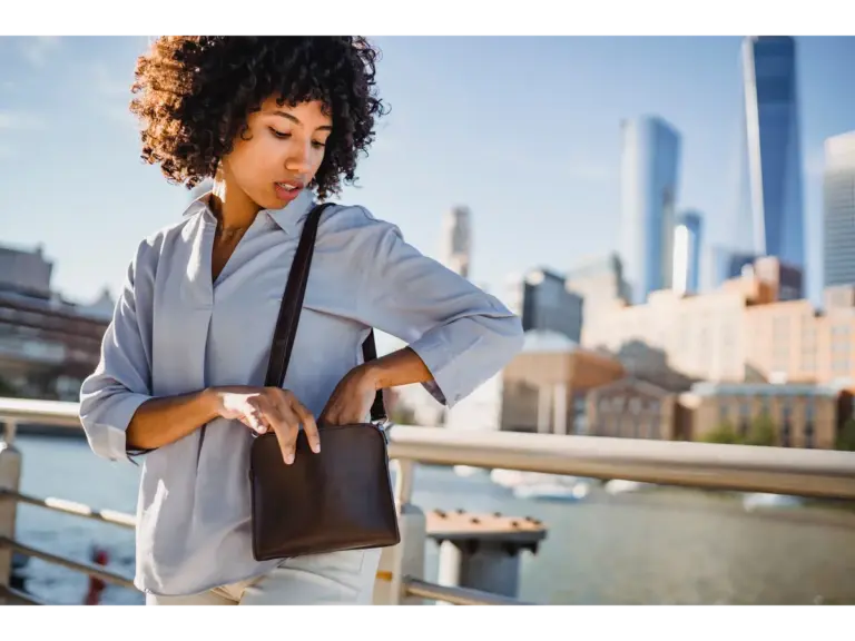 a stylish woman looks into her purse with a city skyline in the background, channeling the same effortless cool that’s made mini bucket bags a go‑to accessory.