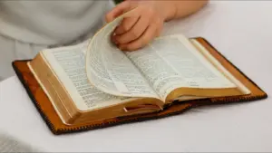 In daily devotional, an open Bible is shown with a hand turning its pages.