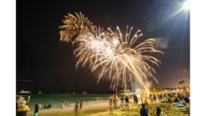 Colorful beach fireworks illuminate the night sky over a packed beach, turning the whole scene into a festive summer moment.