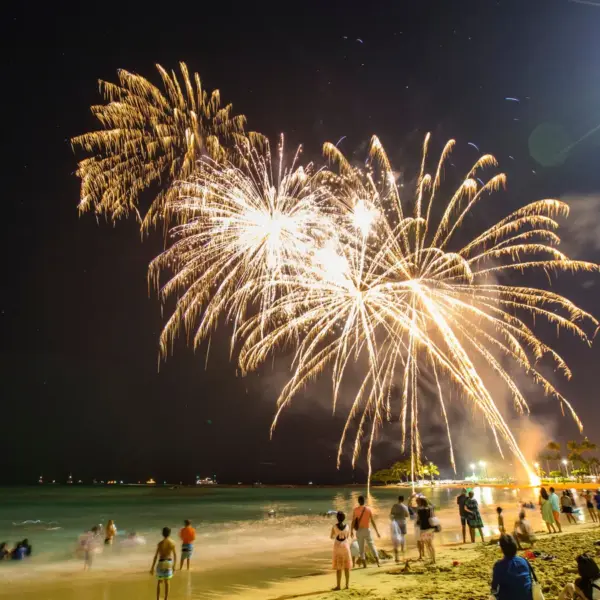 Colorful beach fireworks illuminate the night sky over a packed beach, turning the whole scene into a festive summer moment.