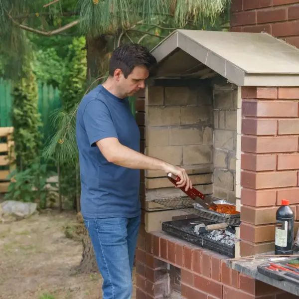 A man grills meat on a brick barbecue in the garden, enjoying outdoor cooking in one of the home’s dedicated BBQ zones.